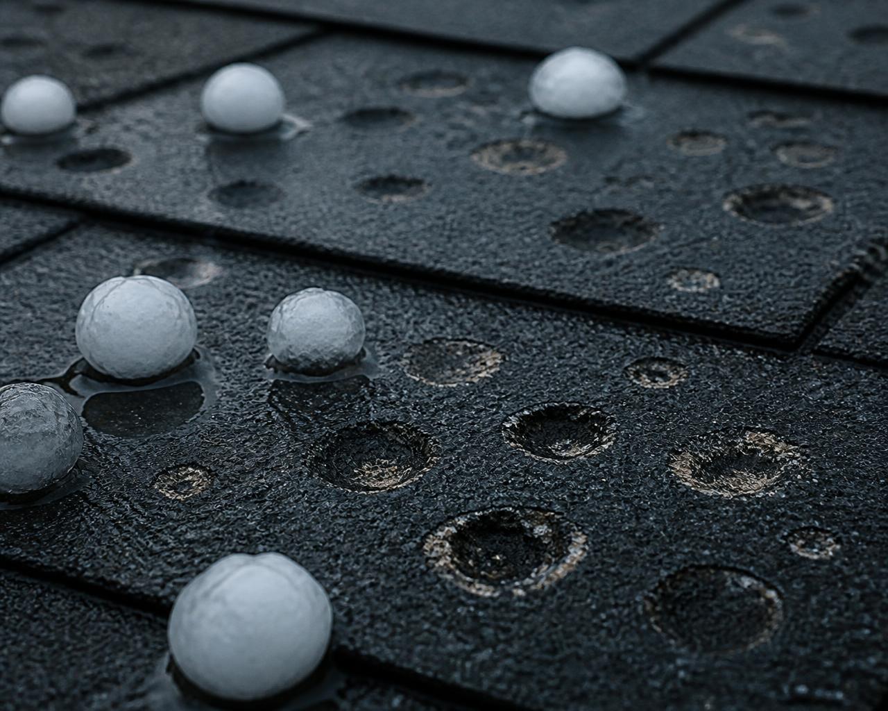 Hail dents and melting hailstones on a dark asphalt shingle roof